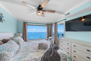 Une chambre à coucher avec un lit, un ventilateur de plafond, une télévision, une commode et une vue sur l’océan.