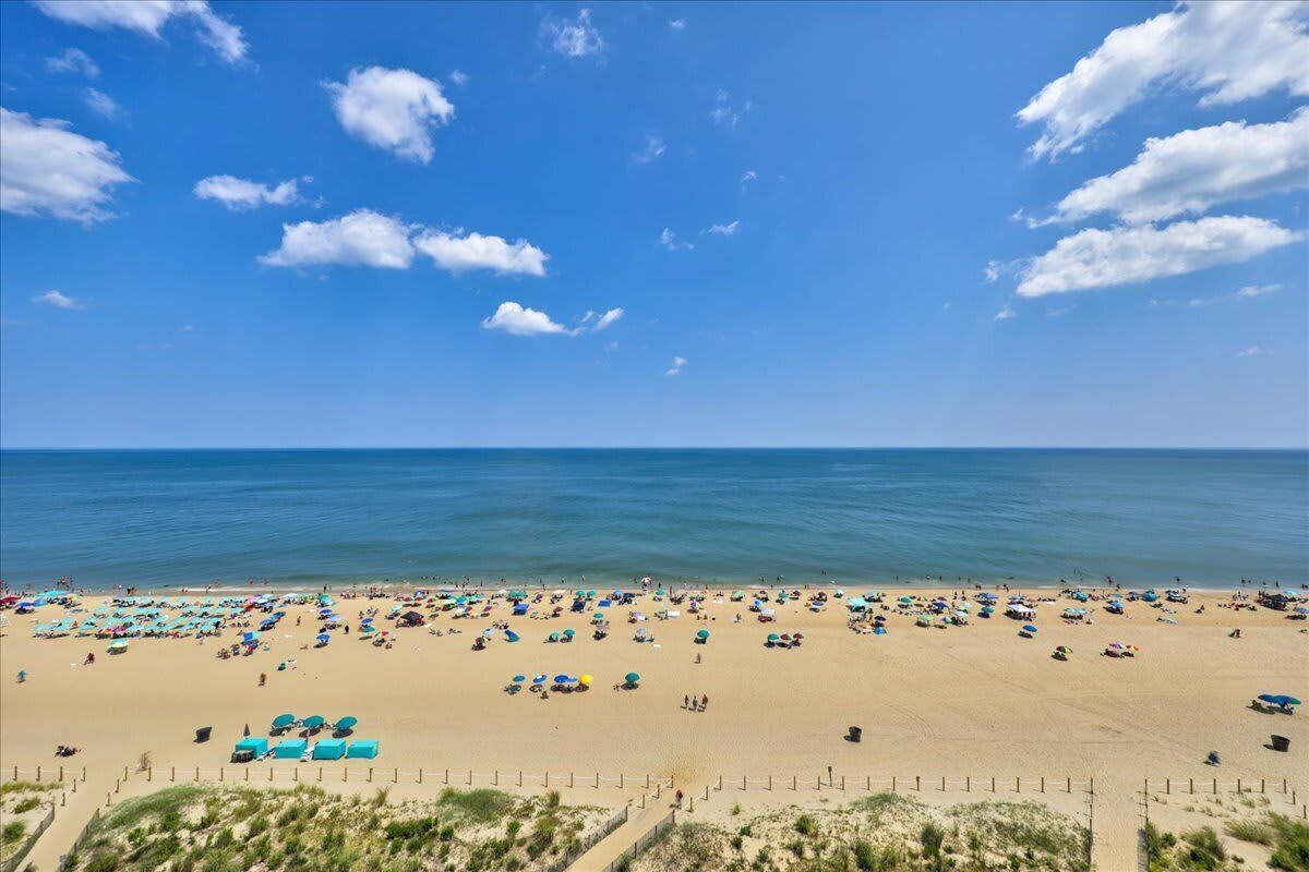 Een strand met parasols en mensen, een heldere lucht en de oceaan.