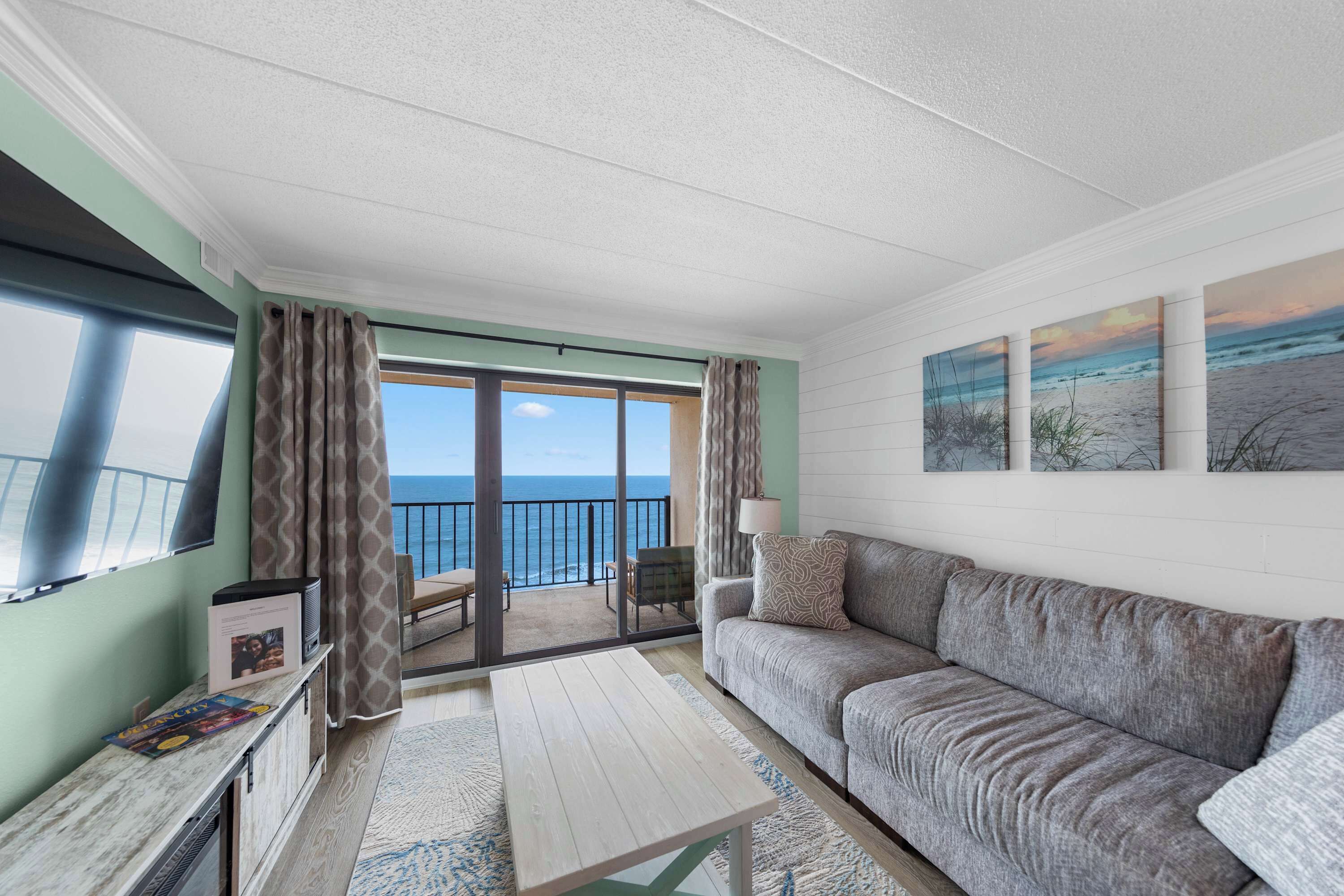 A balcony with a view of the sea, a sofa, a coffee table, and a TV.