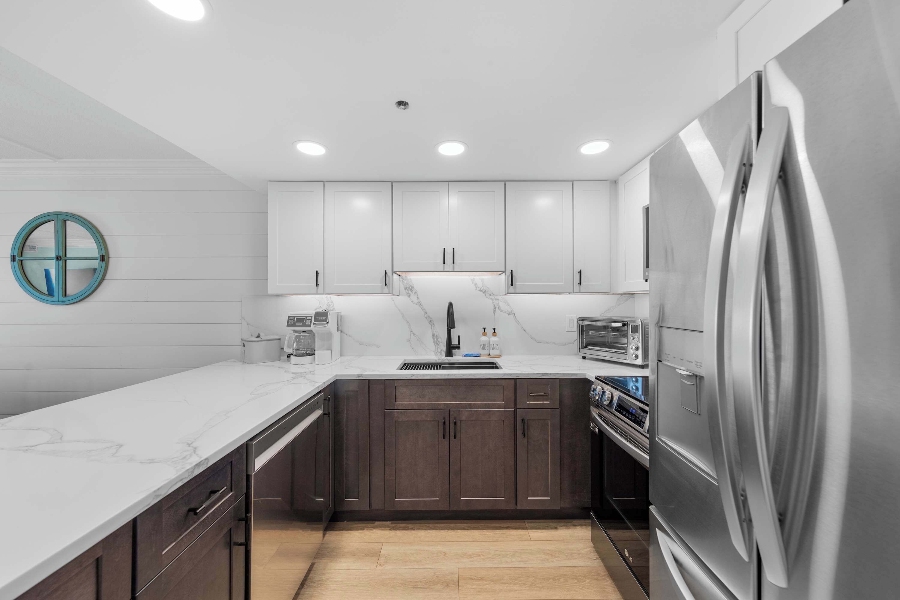 A modern kitchen with dark cabinets, a marble countertop, a stainless steel refrigerator, and a built-in oven.