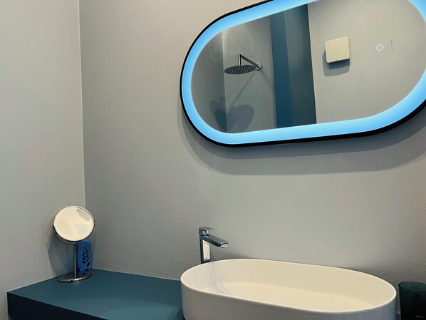 A bathroom with a round mirror, a sink, and a handheld mirror.