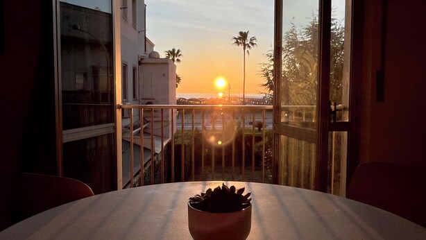 A balcony with a view of the sunset over the water, a table with a potted plant, and a building in the background. - La Casa Sul Pontile (Marina di Vasto)