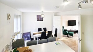 A modern kitchen with a central island, a dining area with chairs, a TV, and a door leading to another room. - Stay Sleep Rest - Brockwell Park (Hull)