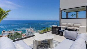 A balcony with a view of the ocean and cityscape, featuring a sofa, a small table, and a chair. - Beautiful condo in delightful Puerto Vallarta with pool, wifi & terrace views! (Puerto Vallarta)