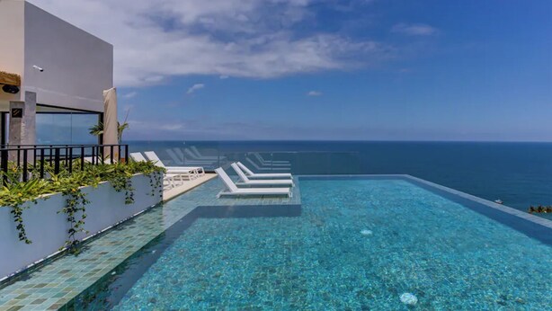 A clear blue infinity pool with white lounge chairs and a view of the ocean. - Beautiful condo in delightful Puerto Vallarta with pool, wifi & terrace views! (Puerto Vallarta)