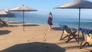 A beach with umbrellas, lounge chairs, and a seagull on one of the umbrellas. - Beautiful condo in delightful Puerto Vallarta with pool, wifi & terrace views! (Puerto Vallarta)