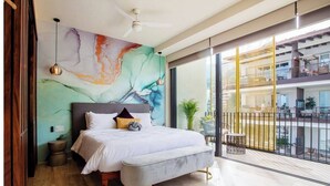A modern bedroom with a large bed, a colorful abstract mural, a ceiling fan, and a balcony with a view of the city. - Beautiful condo in delightful Puerto Vallarta with pool, wifi & terrace views! (Puerto Vallarta)
