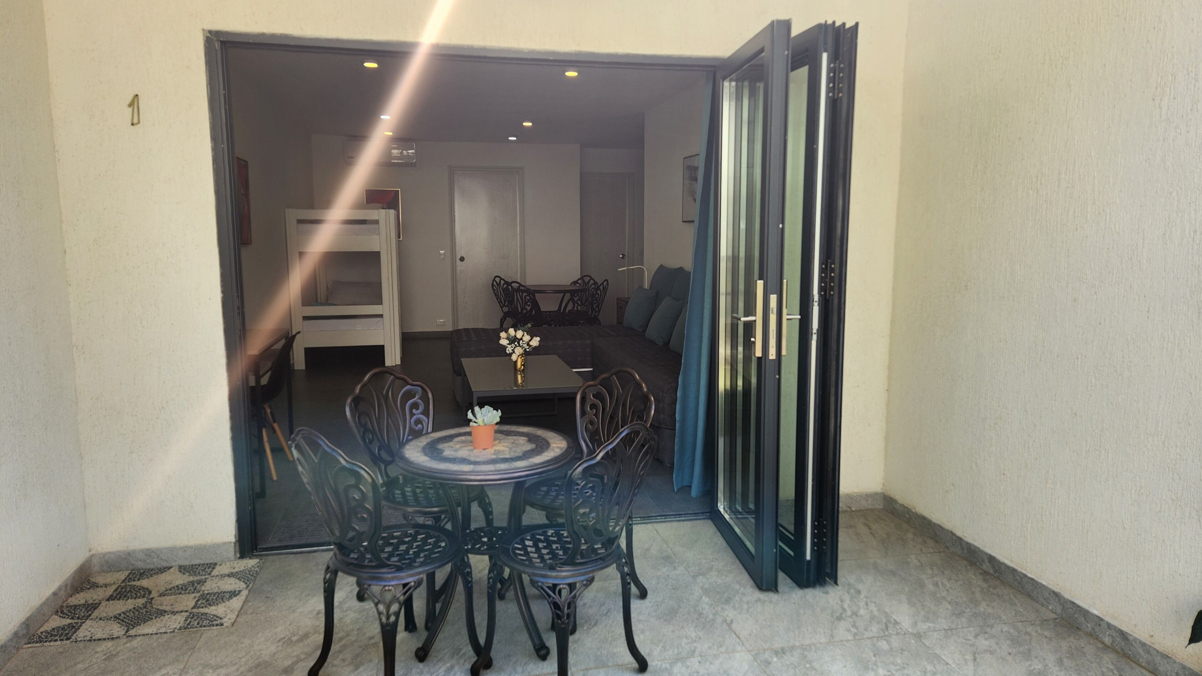 An open door leading to a dining area with a table and chairs, a sofa, and a glass door.
