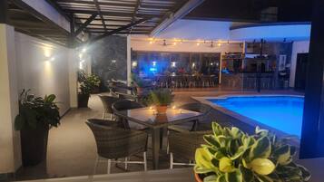 An outdoor patio area with a pool, dining tables, chairs, and potted plants.