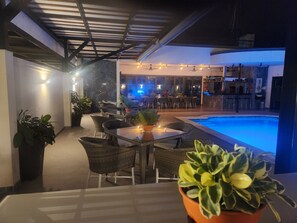 An outdoor patio area with a pool, dining tables, chairs, and potted plants. - Oasis-Dream Holidays - La Petite France (San Bernardino)