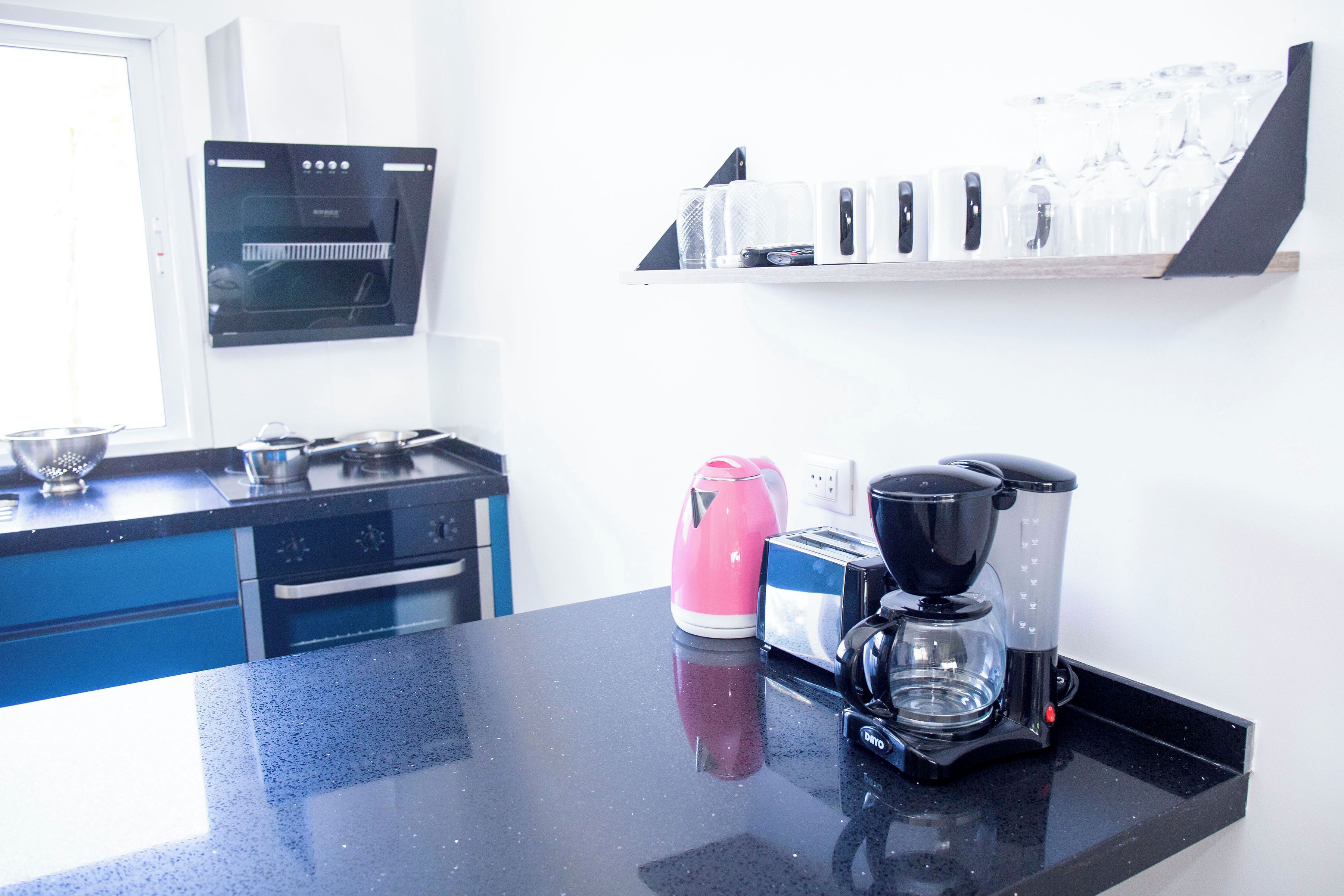Et køkken med en sort bordplade, en pink elkedel, en kaffemaskine og en brødrister.