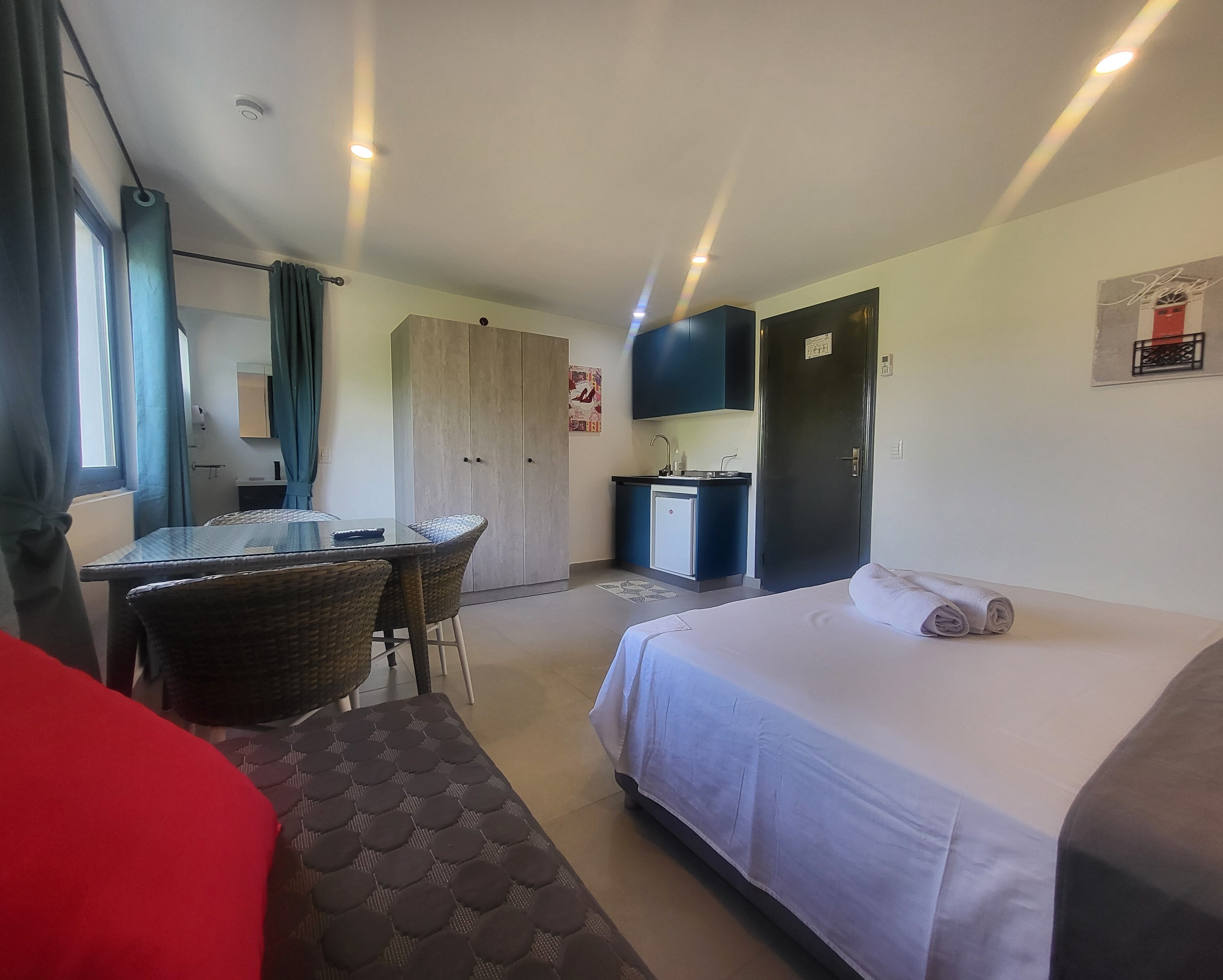 A hotel room with a bed, a dining table with chairs, a kitchenette, and a wardrobe.