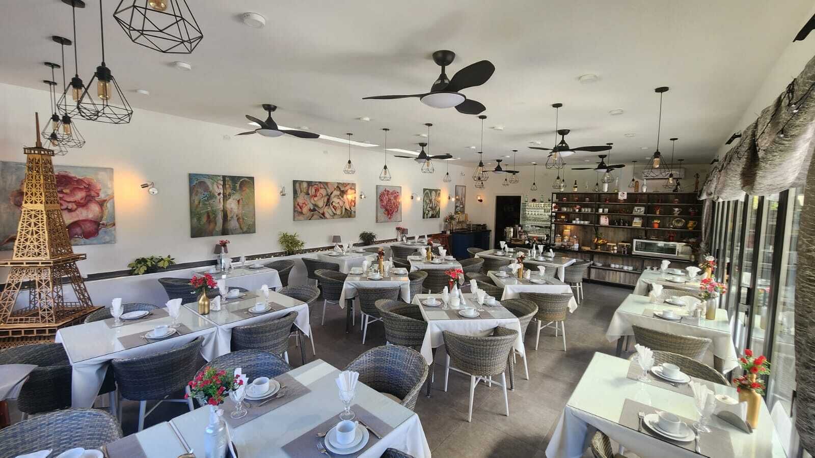 Un restaurante con varias mesas, sillas de mimbre, ventiladores de techo y decoración en las paredes.