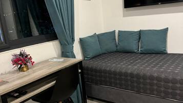 Een slaapkamer met een bed, een bureau, een stoel, een televisie en een airconditioner.