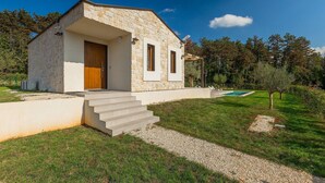 Una casa moderna con fachada de piedra, puerta de madera y una pequeña piscina en el patio trasero.