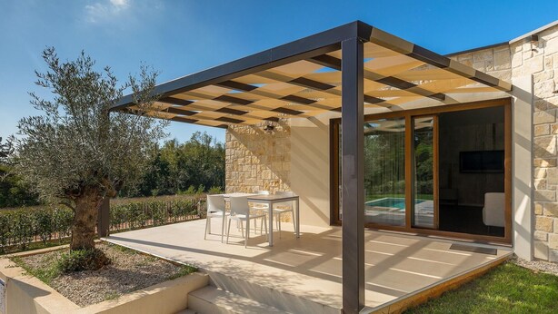 Un patio techado con una mesa y sillas, un muro de piedra y vistas a una piscina.