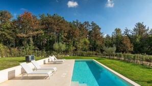 Una piscina rectangular con agua cristalina y azul, rodeada por una terraza blanca con sillas de descanso.