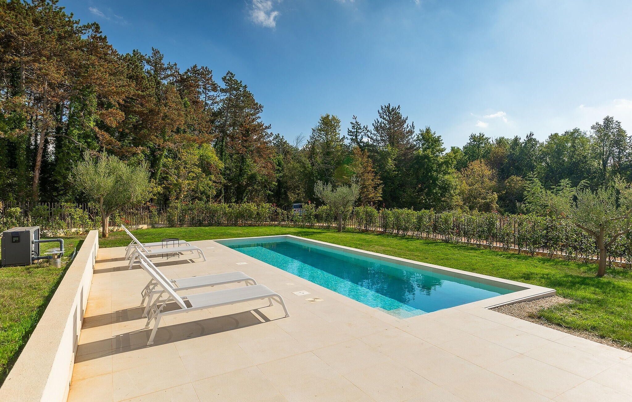 A rectangular swimming pool with a clear blue water surface, surrounded by a paved deck with three lounge chairs and a small utility box to the left.