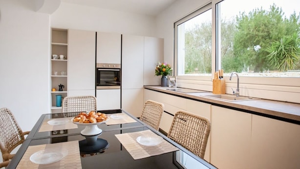 Une cuisine moderne avec une table à manger, des chaises et une fenêtre donnant sur des arbres.
