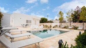 Une piscine avec des chaises longues, un espace patio et un mur en pierre.