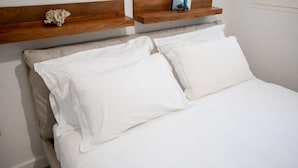 Un lit avec du linge de lit blanc, une tête de lit en bois et une étagère au-dessus, sur laquelle est posé un objet décoratif.