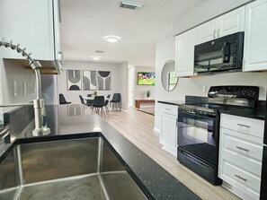 A modern kitchen with a stainless steel sink, black countertops, white cabinets, a black stove, and a microwave.