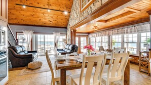 A spacious dining area with a wooden table and chairs, a sofa, and a view of the ocean through large windows. - Waterfront Romulus Getaway w/ Private Dock! (Romulus)