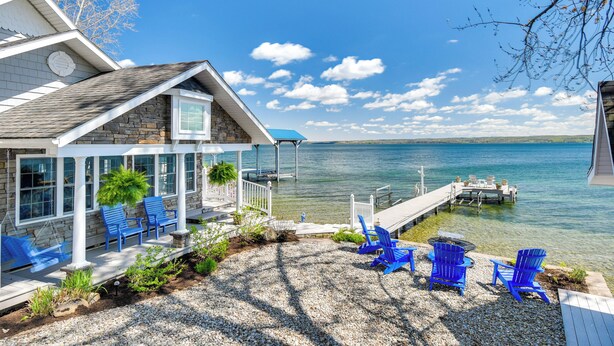 A house with a dock extending into a lake, surrounded by blue Adirondack chairs and a patio area. - Waterfront Romulus Getaway w/ Private Dock! (Romulus)