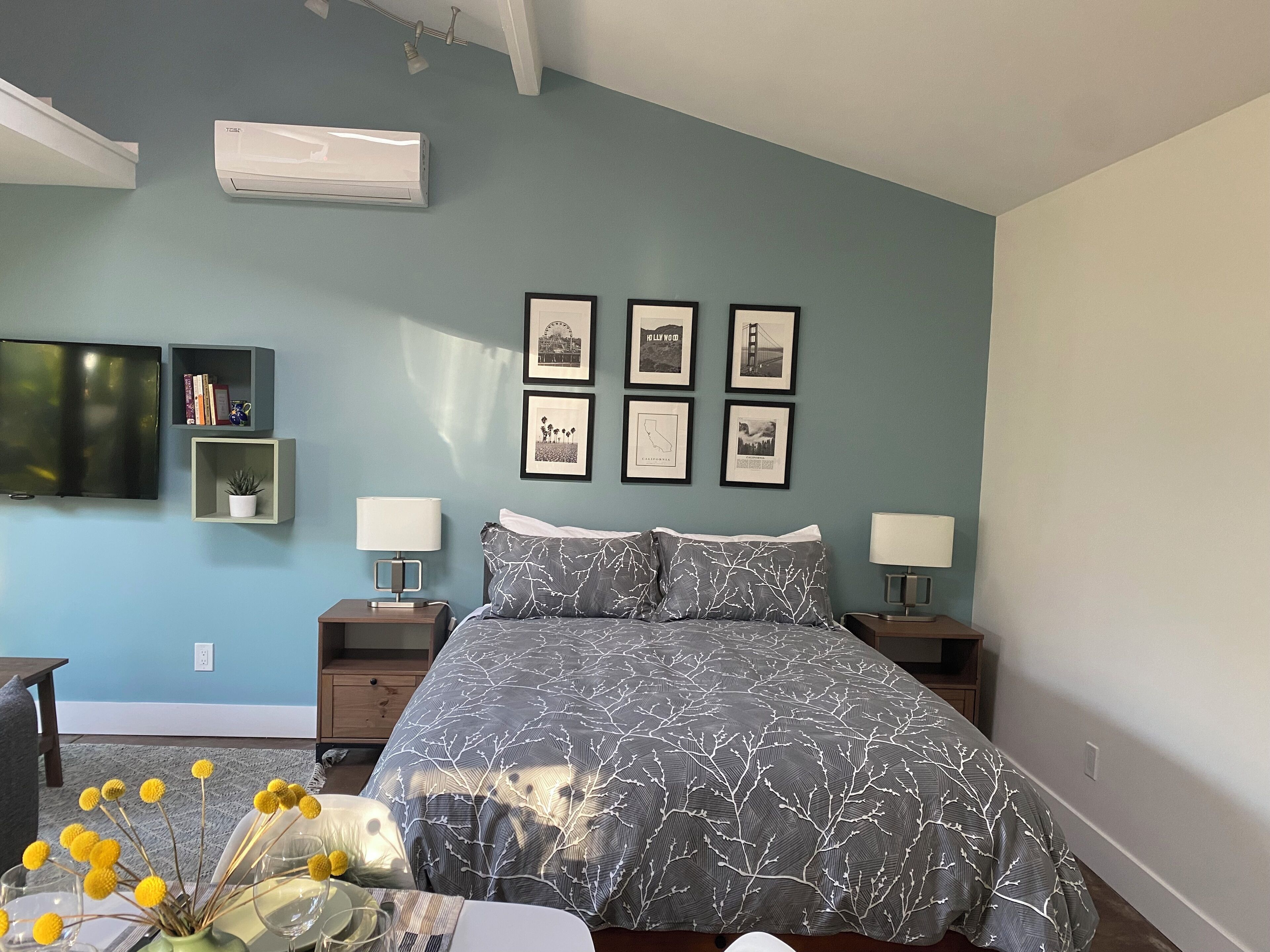 A bedroom with a bed, two bedside tables, a TV, and framed pictures on the wall.