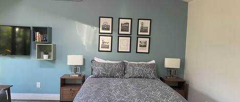 A bedroom with a bed, two bedside tables, a TV, and framed pictures on the wall.
