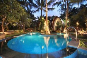 Ein kreisförmiger Pool mit blauem, klarem Wasser, umgeben von Palmen und einem kleinen Gebäude mit Kuppeldach.