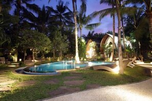 A pool area with a curved edge, surrounded by palm trees and a pathway. - Green Bird Villa (Bali)