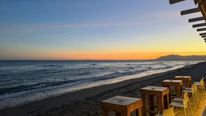 Un espace aménagé avec des tables et des chaises en bois, situé au bord de la plage et offrant une vue sur l’océan.