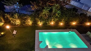 Une piscine rectangulaire à l’eau légèrement verdâtre, entourée d’une pelouse bien entretenue et d’arbres.