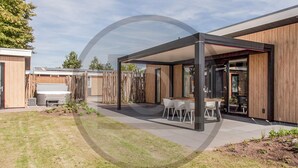 Ein moderner Außenbereich mit Terrasse, überdachtem Sitzbereich, Esstisch und Stühlen sowie Holzzaun.