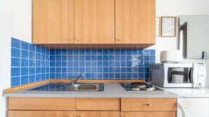 Et køkken med træskabe, et backsplash med blå fliser, en stålvask, en mikrobølgeovn og en brødrister.
