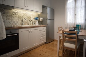A kitchen with white cabinets, a stainless steel refrigerator, a wooden dining table, and a chair.