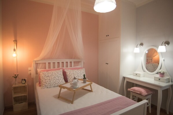 A bedroom with a bed, bedside table, vanity with mirror, and a hanging canopy.
