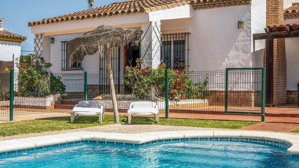 A house with a swimming pool, a patio with chairs, and a fenced garden area. - Holiday Home 'Chalet Villa Ariza' with Private Pool, Private Garden and Wi-Fi (Cádiz)