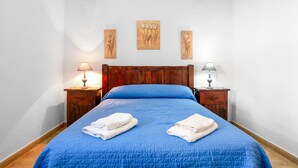 A room with a wooden headboard, a blue bedspread, two bedside tables with lamps, and three wall-mounted paintings. - Holiday Home 'Chalet Villa Ariza' with Private Pool, Private Garden and Wi-Fi (Cádiz)