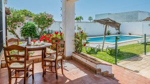 A covered patio with a table and chairs, a pool, and a garden with plants and flowers. - Holiday Home 'Chalet Villa Ariza' with Private Pool, Private Garden and Wi-Fi (Cádiz)