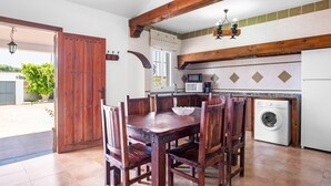 A kitchen with a wooden table and chairs, a washing machine, and a large wooden door. - Holiday Home 'Chalet Villa Ariza' with Private Pool, Private Garden and Wi-Fi (Cádiz)