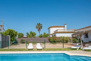 A swimming pool with lounge chairs, a white building with a tiled roof, and a fenced garden area.