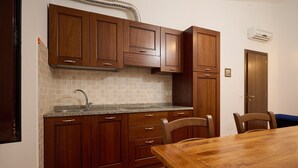 A kitchen with wooden cabinets, a granite countertop, a sink, and a dining table with chairs. - Apartment 'Antichi Palmenti - Mirto' with Shared Garden and Air Conditioning (San Vincenzo)