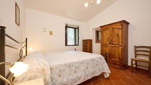 A bedroom with a bed, a wooden wardrobe, a chair, a desk, a lamp, and a window. - Apartment 'Antichi Palmenti - Mirto' with Shared Garden and Air Conditioning (San Vincenzo)