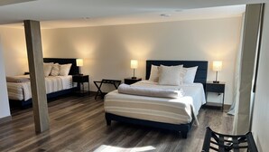 A modern hotel room with a large bed, two bedside tables with lamps, a wooden floor, and a black chair.