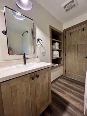 Un baño con un espejo grande, un lavabo, un perchero para toallas y un armario de madera.