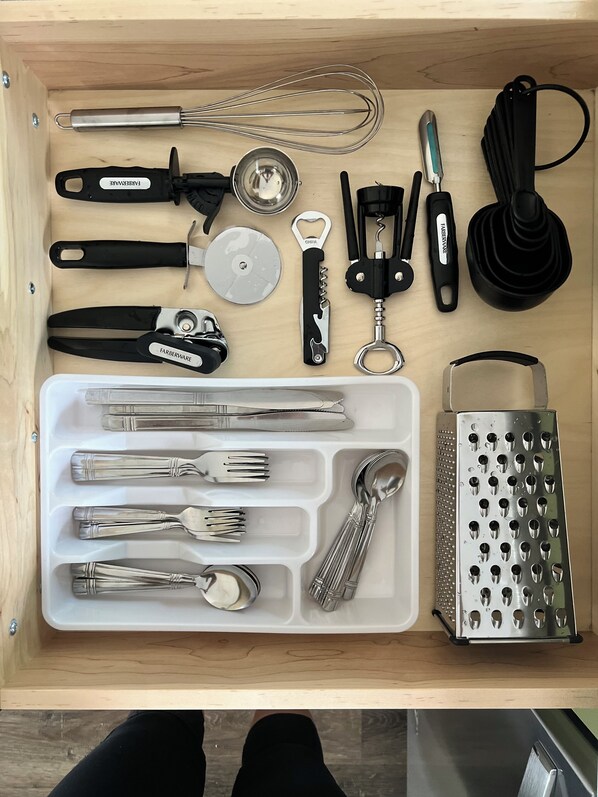 A drawer containing various kitchen utensils and tools, including whisks, a grater, and a knife set.