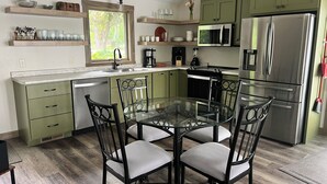 A modern kitchen with green cabinets, stainless steel appliances, and a glass dining table with chairs.