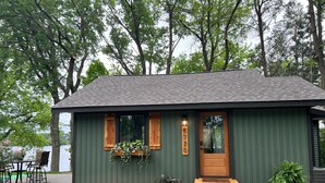 A small, single-story house with a dark green exterior, a wooden front door, and a small porch.